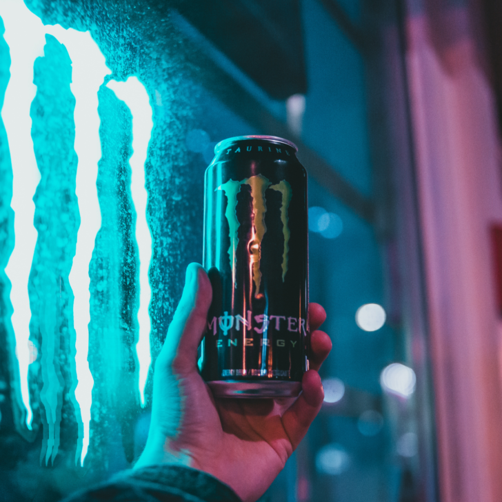 close up of a monster energy drink with a monster sign lit up beside it