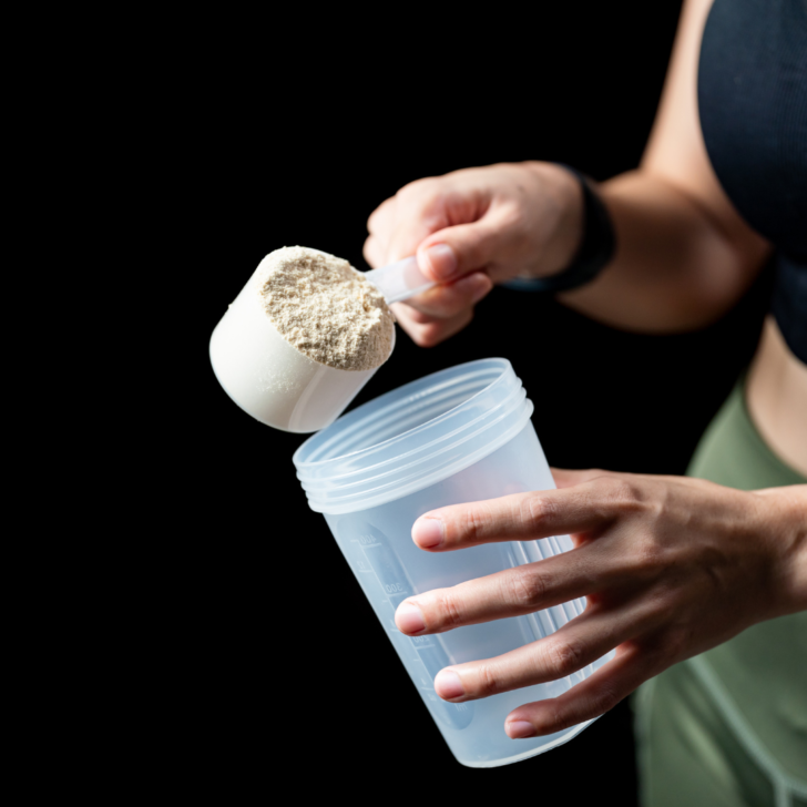 woman poring protein powder into a plastic bottle